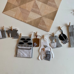 Puede incluir: Un banner de juego de cocina de fieltro con varios artículos de cocina, que incluyen una estufa, un horno, una olla, una tabla de cortar, un delantal, una batidora y una sartén. Los artículos están unidos a una cuerda blanca con pinzas de madera.
