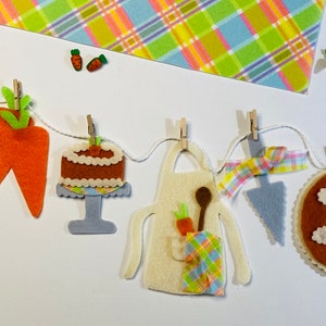 Puede incluir: Una pancarta de fieltro con una zanahoria, un pastel, un delantal, un pastel y un conejito. La pancarta está colgada con pinzas para la ropa y es perfecta para una fiesta de primavera o de Pascua.