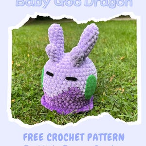 Op de afbeelding: Een handgemaakte, pluche, lavendelkleurige Baby Goo Dragon, met groene accenten en zwarte ogen, staat op gras. De tekst "Baby Goo Dragon" staat boven de draak. Daaronder staat "FREE CROCHET PATTERN By Little Bunny Garden."