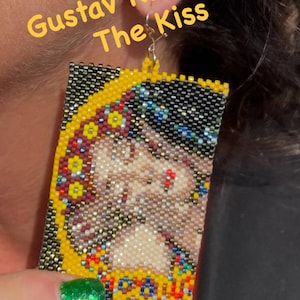 May include: Handmade beaded earrings featuring a rectangular design with the image of Gustav Klimt's "The Kiss." The earrings have a yellow border and a detailed mosaic of colors. The text "Gustav Klimt The Kiss" is visible.