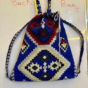 May include: A handmade blue backpack with a geometric pattern in red, black, and white. The bag has drawstring closure and shoulder straps. The word "Back Bag" is written in red on the top left and right. The word "Handmade" is written in red at the bottom.