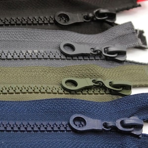 May include: Close-up of four different zipper tapes with metal sliders. The tapes are in various colours: black, grey, green, and blue.