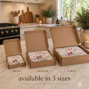 May include: Three open cardboard boxes, labeled Small, Medium, and Large, each containing a floral-patterned item. The boxes are on a countertop, with the text "available in 3 sizes" below. The floral pattern includes red and orange accents.