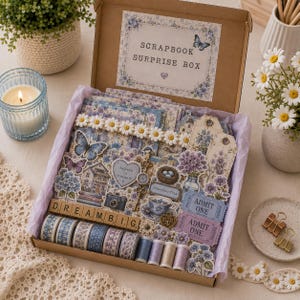 May include: A cardboard scrapbook surprise box filled with floral and butterfly-themed paper ephemera, including washi tape rolls, die-cut shapes, tags, and two purple admit one tickets. The box lid features the text SCRAPBOOK SURPRISE BOX.