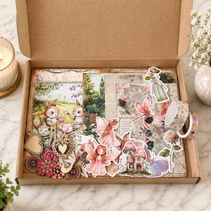 May include: A craft box filled with fairy-themed scrapbook supplies. Includes decorative paper, stickers of fairies, mushrooms, and flowers, wooden embellishments, and floral washi tape. The box is open, revealing the contents.