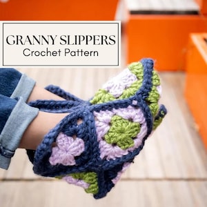May include: A pair of handmade crochet slippers in a granny square pattern. The slippers feature a combination of lavender, green, and white squares, outlined in navy blue yarn. The text "GRANNY SLIPPERS Crochet Pattern" is in a white rectangle.