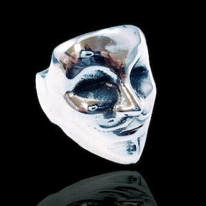 Puede incluir: Un anillo de plata con un diseño detallado de una cara con una máscara. El anillo está hecho a mano por ezi zino.