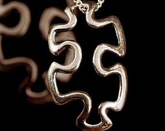 Puede incluir: Un collar de cadena de plata con un colgante de pieza de rompecabezas de plata. El colgante es un simple contorno de una pieza de rompecabezas.