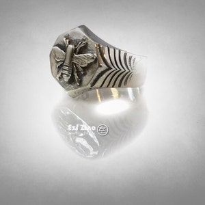 May include: A silver ring with a hexagonal design featuring a detailed bee sculpture. The band has a textured pattern.