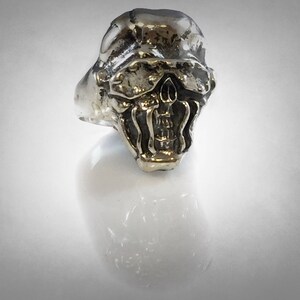 Pu&ograve; includere: Un anello d'argento con un designo di teschio dettagliato. Il teschio ha un'espressione minacciosa con denti affilati e la fronte aggrottata.