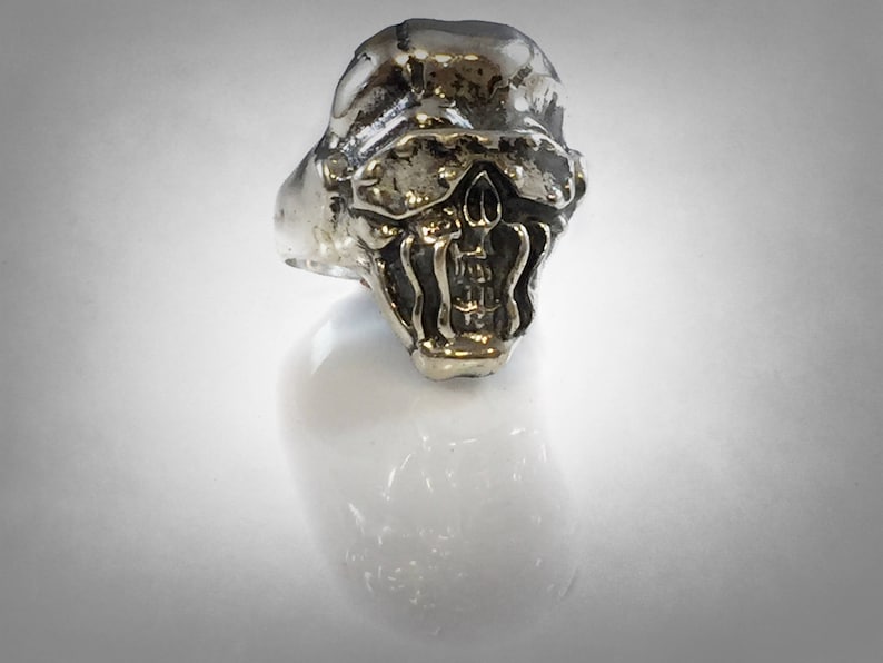 Pu&ograve; includere: Un anello d'argento con un designo di teschio dettagliato. Il teschio ha un'espressione minacciosa con denti affilati e la fronte aggrottata.