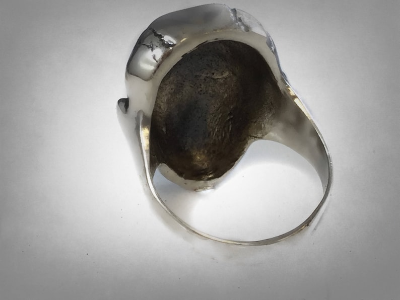 Pu&ograve; includere: Anello d'argento con un design a forma di teschio. L'anello &egrave; mostrato dall'interno, rivelando la fascia liscia in argento.