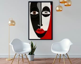 May include: Abstract art print featuring a stylized face divided vertically. One side is black, the other white and red. The face has a brown eye and a gray eye, with red lips. The artwork is framed in black and hangs on a white wall.