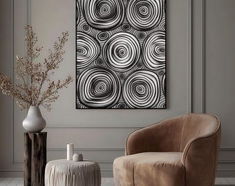 May include: Abstract black and white artwork featuring a pattern of concentric circles. The framed art hangs above a brown armchair, with a small ottoman and a vase of dried branches in the foreground. The room has a neutral color palette.