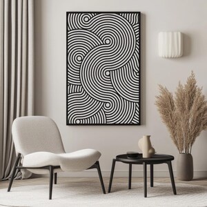 May include: A black and white abstract art piece with a geometric design of concentric circles. The artwork is framed and hangs on a neutral-colored wall. The room also features a modern chair, a small table, and decorative plants.