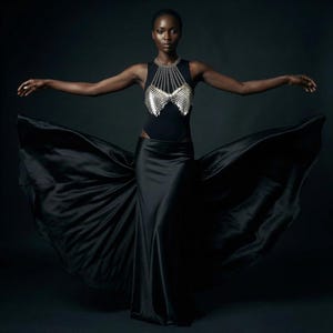 May include: A woman in a black bodysuit and skirt with a silver chainmail top. The skirt flows dramatically, creating a dynamic image against a dark background. The outfit is elegant and striking.