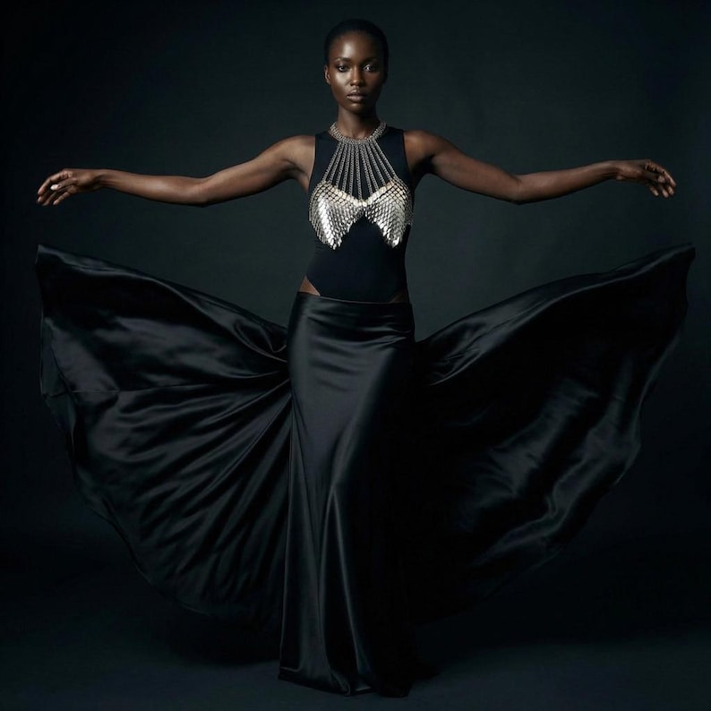 May include: A woman in a black bodysuit and skirt with a silver chainmail top. The skirt flows dramatically, creating a dynamic image against a dark background. The outfit is elegant and striking.