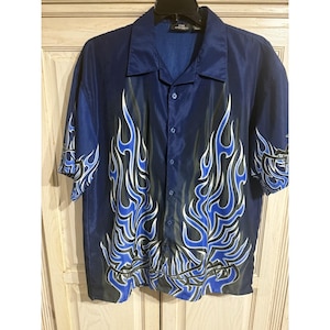 May include: A short-sleeved, button-down shirt in navy blue with a flame design in blue, white, and black. The shirt has a classic collar and a relaxed fit, suitable for casual wear.
