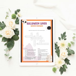 May include: A digital tablet displaying a Halloween Lover Wedding Crossword puzzle. The page features a skull icon, a spider graphic, and a ghost illustration. The crossword grid is centered with numbered clues listed below in two columns titled Across and Down.