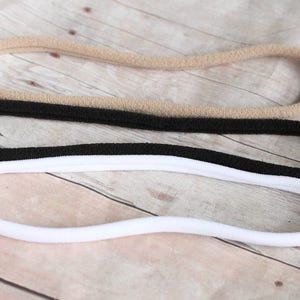 Pode incluir: Tr&ecirc;s el&aacute;sticos de cabelo em cores diferentes: bege, preto e branco. Os el&aacute;sticos de cabelo s&atilde;o feitos de um material macio e el&aacute;stico.