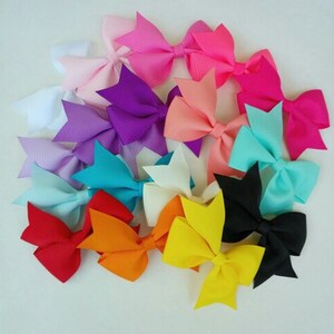 May include: A collection of 14 colorful hair bows in various colors, including pink, purple, blue, white, yellow, orange, and black. The bows are made of grosgrain ribbon and are tied in a classic bow shape.