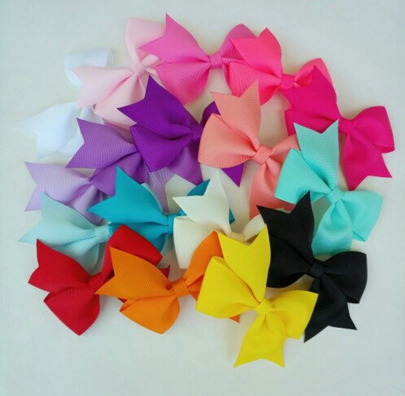 May include: A collection of 14 colorful hair bows in various colors, including pink, purple, blue, white, yellow, orange, and black. The bows are made of grosgrain ribbon and are tied in a classic bow shape.