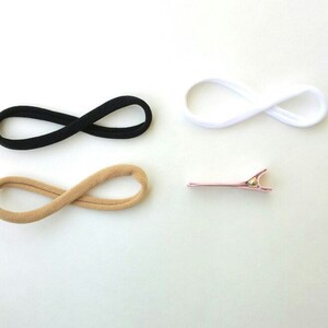 May include: Three hair ties in black, beige, and white, and a pink hair clip.