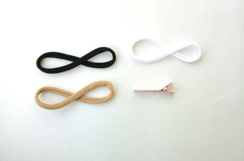 May include: Three hair ties in black, beige, and white, and a pink hair clip.