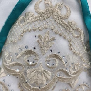 May include: White fabric with a gold embroidered design featuring a floral motif. The embroidery is accented with small, clear rhinestones.