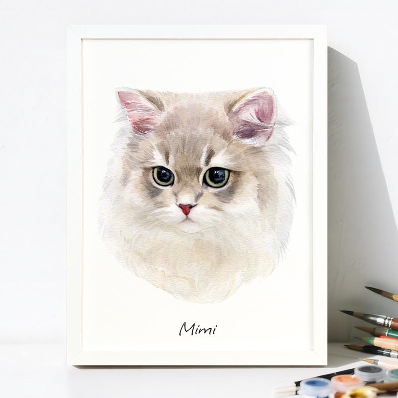 May include: A framed watercolor painting of a cat's face. The cat has light gray and white fur, green eyes, and a pink nose. The name "Mimi" is written in cursive below the cat's portrait.