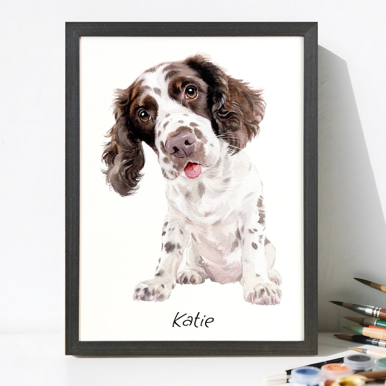 May include: A framed watercolor painting of a Springer Spaniel dog. The dog has brown and white fur, with a pink tongue sticking out. The dog is sitting and looking at the viewer. The name "Katie" is written at the bottom.