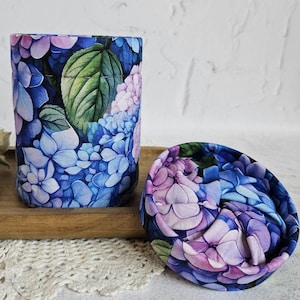 May include: A white ceramic mug with a black handle and the text "But First, Coffee" in a bold, black font. The mug is set against a neutral background, highlighting its simple design.