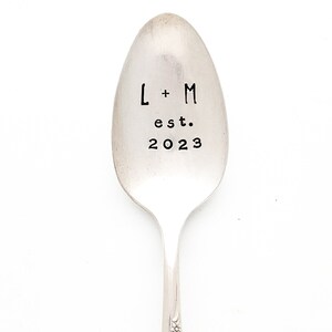 May include: A silver spoon with the text "L + M est. 2023" engraved on the front.