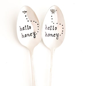 May include: Two silver spoons with black lettering that reads "hello honey."  Each spoon has a small bee charm at the top with a dotted line leading to the text.