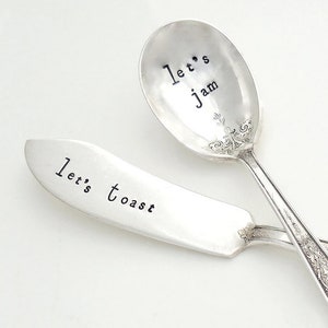 May include: A set of two vintage silver spoons with engraved sayings. The butter knife says "Let's Toast" and the spoon says "Let's Jam".