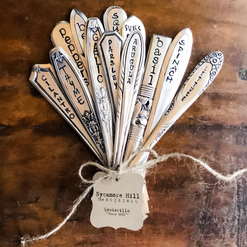 May include: A set of vintage silverware garden markers with names of herbs and vegetables written on them, tied together with twine and a tag that reads "Sycamore Hill The ORIGINAL Louisville Since 2010."