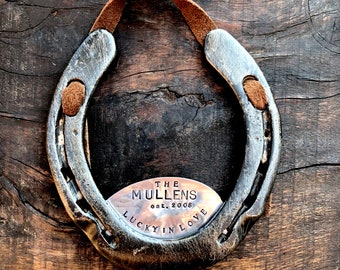 May include: A silver horseshoe with a leather strap and a copper plaque that reads "The Mullens est. 2008 Lucky in Love".