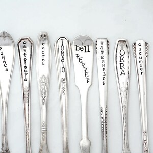 May include: Nine silver spoons with engraved names of vegetables, including spinach, carrot, tomato, bell pepper, watermelon, okra, and cucumber.