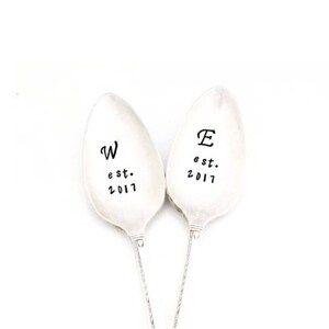 May include: Two silver spoons with the letters "W" and "E" engraved on them. The spoons also have the text "est. 2017" engraved on them.