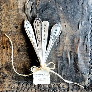 May include: Set of five silver spoons with engraved names of herbs: Thyme, Chives, Oregano, Sage. The spoons are tied together with twine and a tag that reads "Sycamore Hill The Original Louisville Since 2019."