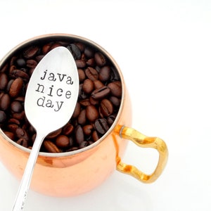 May include: A copper mug filled with coffee beans and a silver spoon with the text "java nice day" engraved on it.