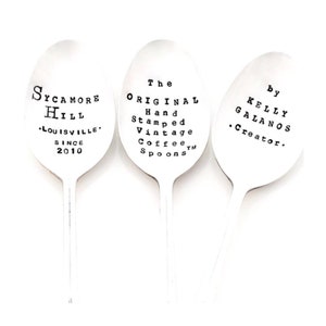 May include: Three silver spoons with black text. The first spoon says "Sycamore Hill • Louisville • Since 2010". The second spoon says "The Original Hand Stamped Vintage Coffee™ Spoons". The third spoon says "By Kelly Galanos • Creator."