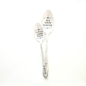 May include: Two silver spoons with black engraved text. The larger spoon says "BIG SPOON GARRETTE" and the smaller spoon says "LITTLE SPOON ELISA".