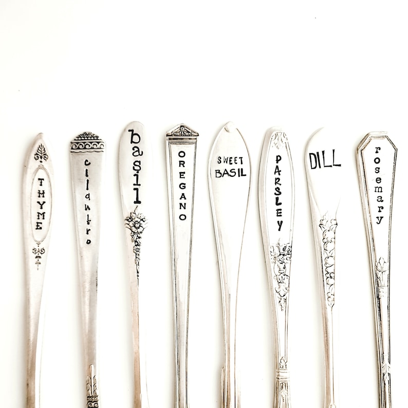 May include: Nine silver spoons with engraved names of herbs, including Thyme, Cilantro, Basil, Oregano, Sweet Basil, Parsley, Dill, and Rosemary.