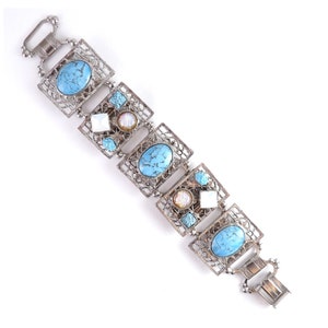 May include: Silver-toned bracelet featuring turquoise and white gemstones. The bracelet has an openwork design with square and oval shapes. The clasp is a fold-over style. The bracelet is a piece of jewelry.