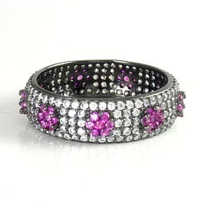 May include: A black band ring with a row of small white stones and four pink flower-shaped stones.