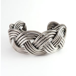 May include: Silver-toned cuff bracelet with a woven design. The bracelet features multiple strands of metal intricately intertwined to create a textured, openwork pattern. The ends of the bracelet are slightly curved.