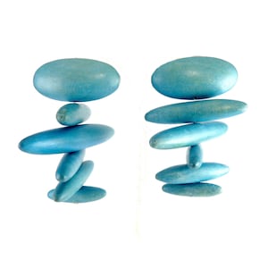 May include: Two pairs of blue wooden earrings, each composed of stacked, oval-shaped pieces. The earrings have a smooth, slightly weathered appearance and are set against a white background. The design is minimalist and abstract.