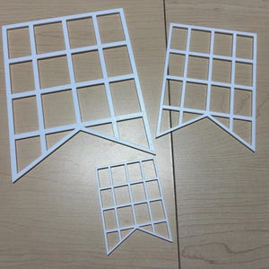 May include: Three white, flat, grid-patterned pennant shapes of varying sizes. Each piece features a rectangular frame divided into smaller squares by thin horizontal and vertical bars, with a triangular cutout at the bottom edge.