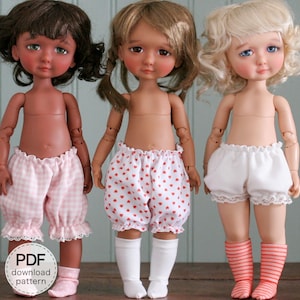 May include: Three dolls wearing different patterned bloomers. The doll on the left is wearing pink and white gingham bloomers, the middle doll is wearing red and white heart-patterned bloomers, and the doll on the right is wearing white bloomers with lace trim. All three dolls are wearing socks.